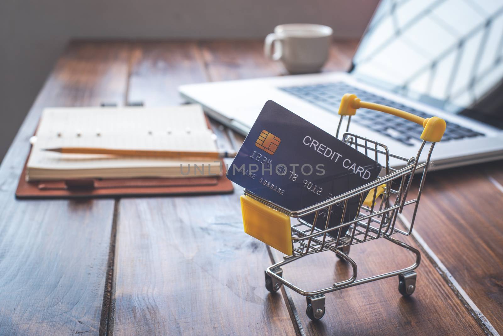 Small shopping cart with credit card inside and behind is business on desk - concept use credit for shopping.