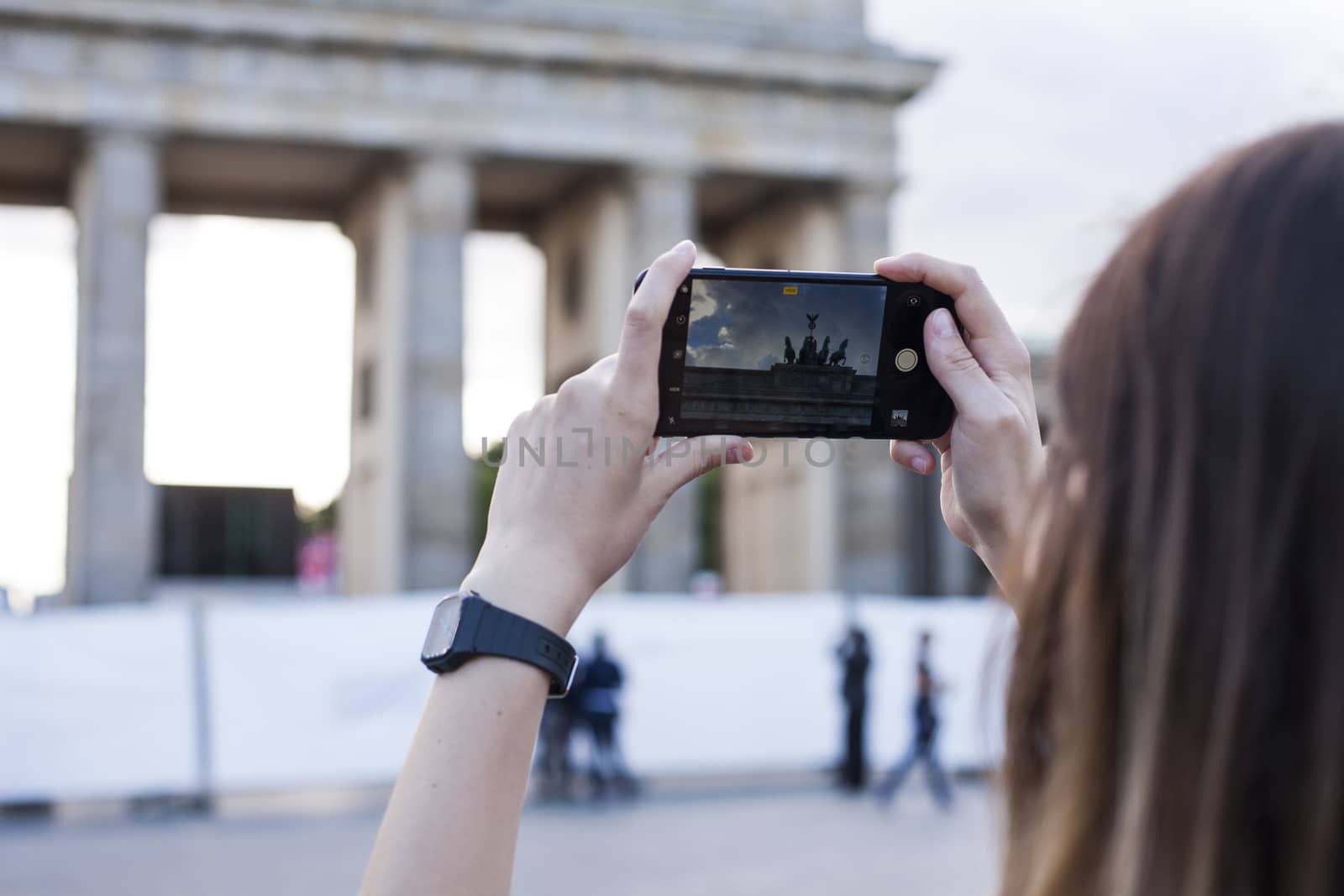 Hands holding phone mobile and takes pictures of famous historical tourist sites. The Brandenburg Gate neoclassical monument in Berlin.