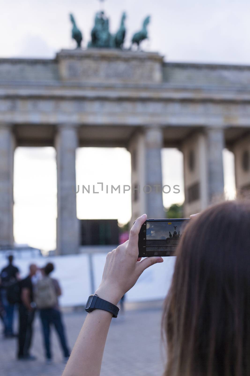 Hands holding phone mobile and takes pictures of famous historical tourist sites. The Brandenburg Gate neoclassical monument in Berlin.