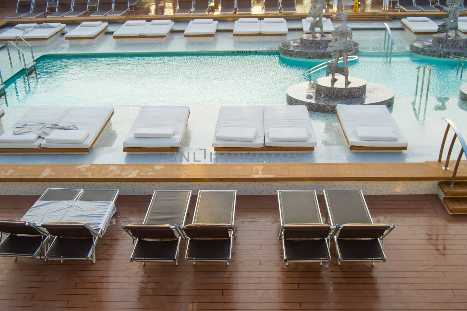Top view of the luxurious pool with empty sun beds on the open deck of a modern cruise liner.