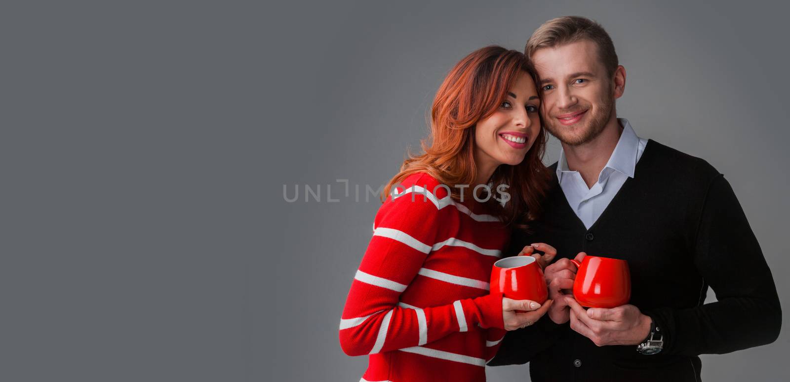 Beautiful young couple in love looking to each other holding red cups , Valentines day concept