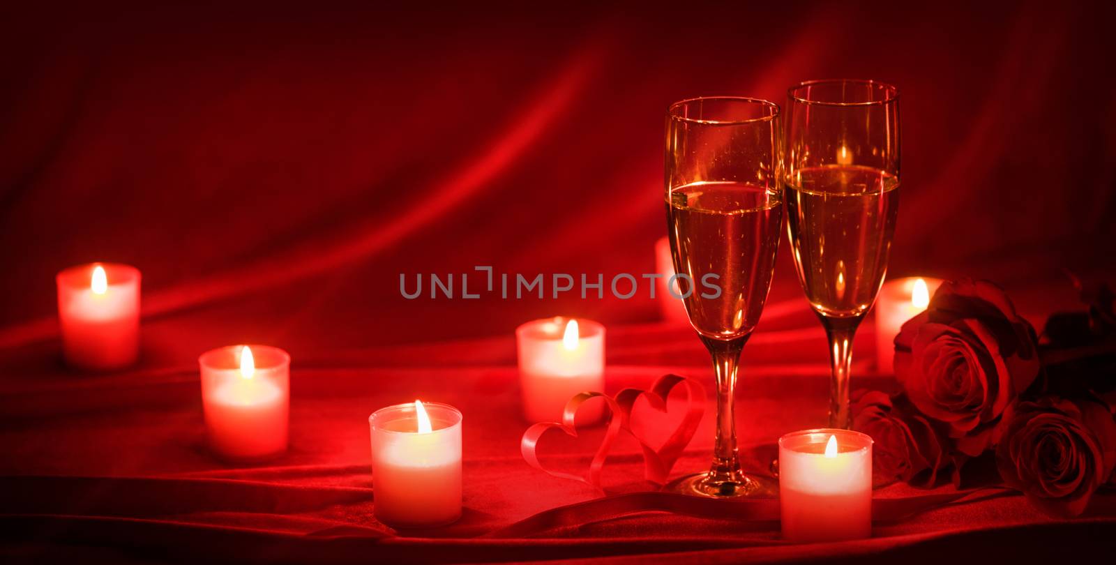 Valentines day celebration, glasses of champagne, candles, roses and hearts on red silk