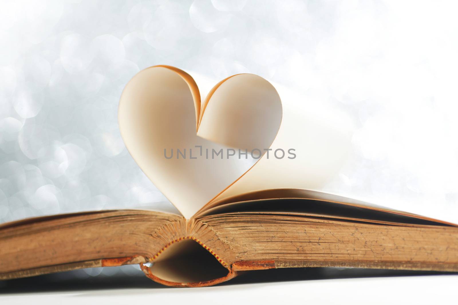 Pages of open book rolled in heart shape on glitter background
