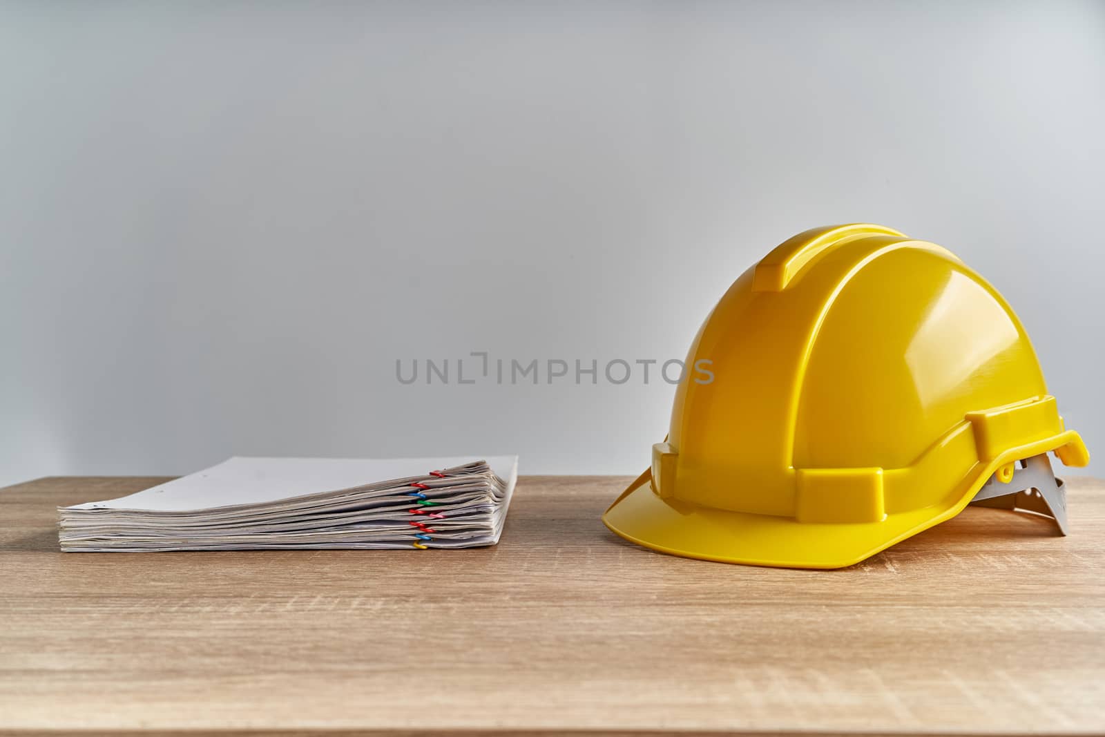 Stack document of report and receipt with colorful paperclip with yellow engineer hat on wooden table with white background and copy space. Industrial successful concept photography.