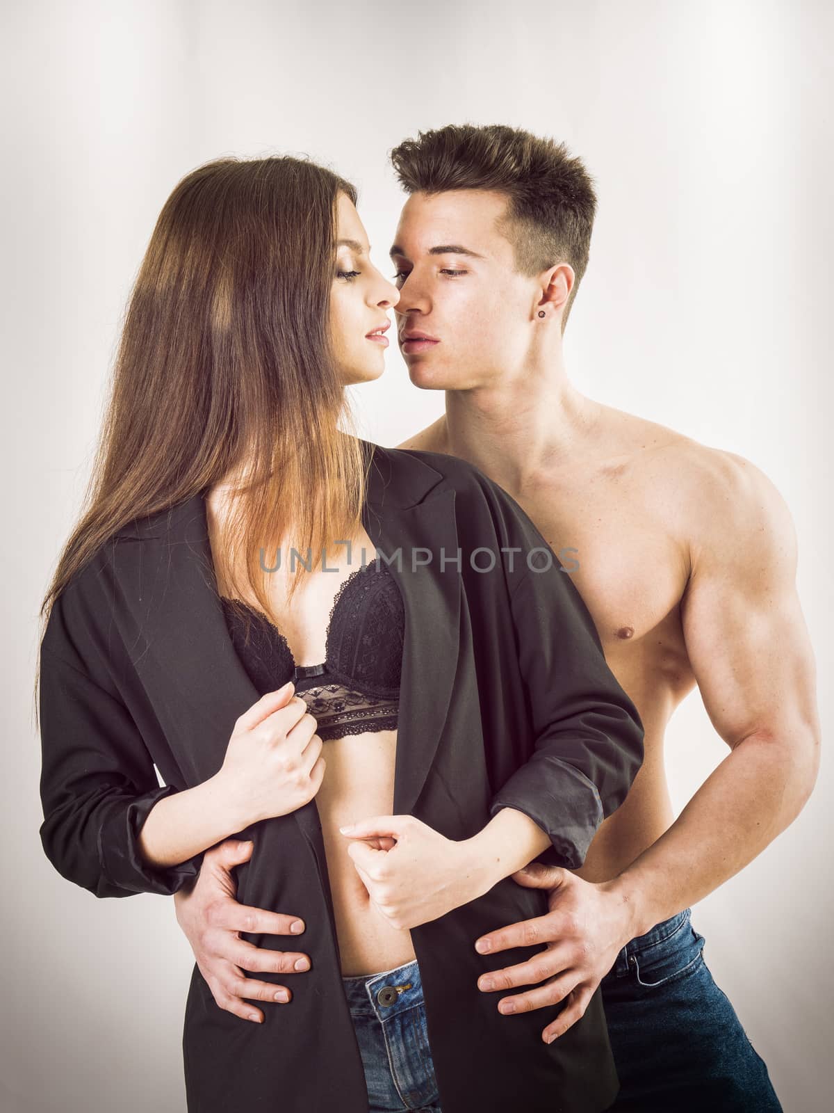 Romantic couple embracing in studio shot, just about to kiss, man is muscular and shirtless, woman is showing bra under open shirt