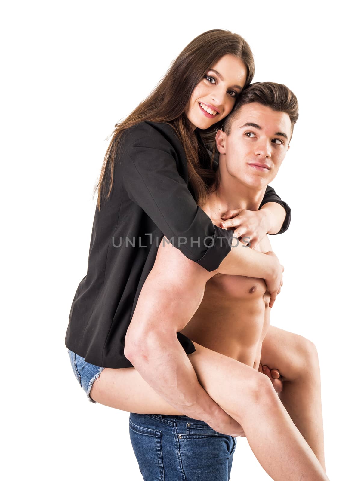 Romantic young couple, muscular shirtless man and pretty woman doing piggyback on him, isolated in studio shot, looking at camera