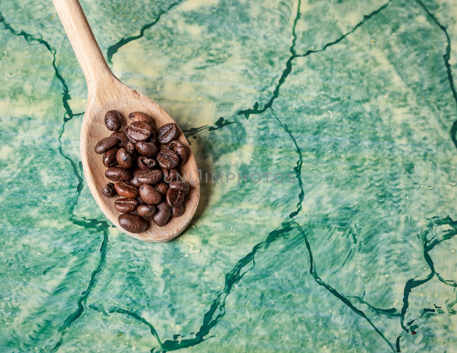 Wooden spoon with coffee beans on top, background green surface.