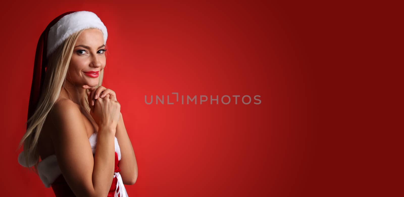 Portrait of a happy attractive young woman posing in red santa claus costume on red background with copy space