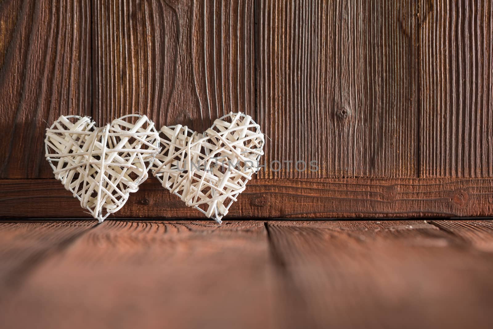 Two wicker hearts on brown wooden background