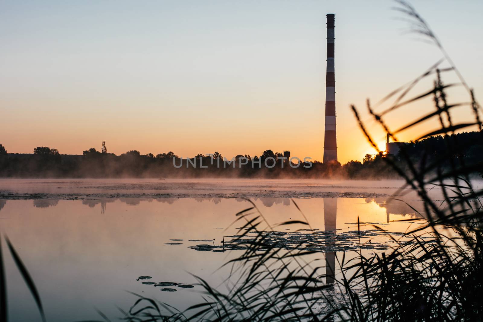 sunrise over the lake and a factory chimney