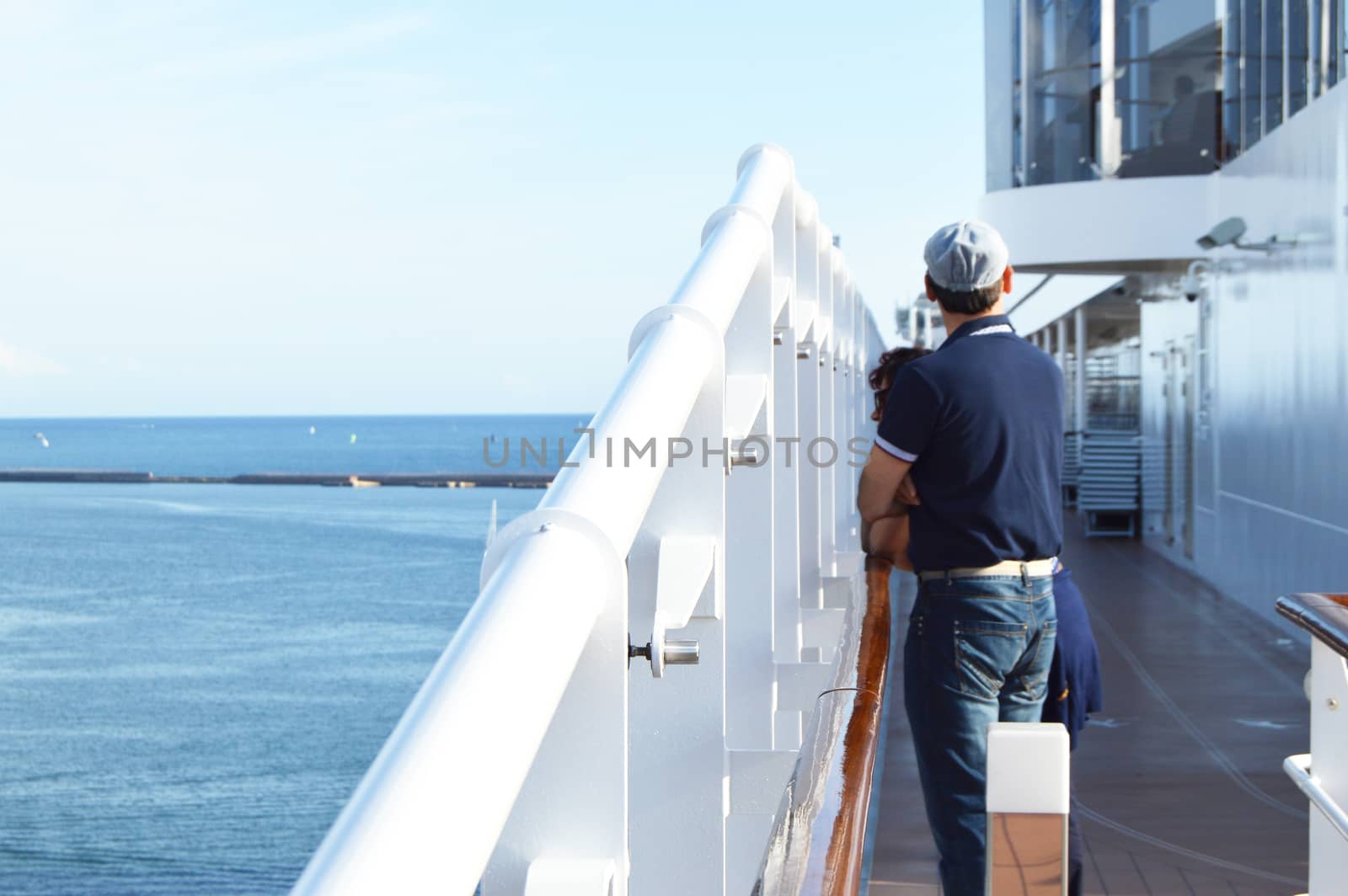 A man stands on the deck of a cruise ship and looks at the shore on a Sunny day by claire_lucia