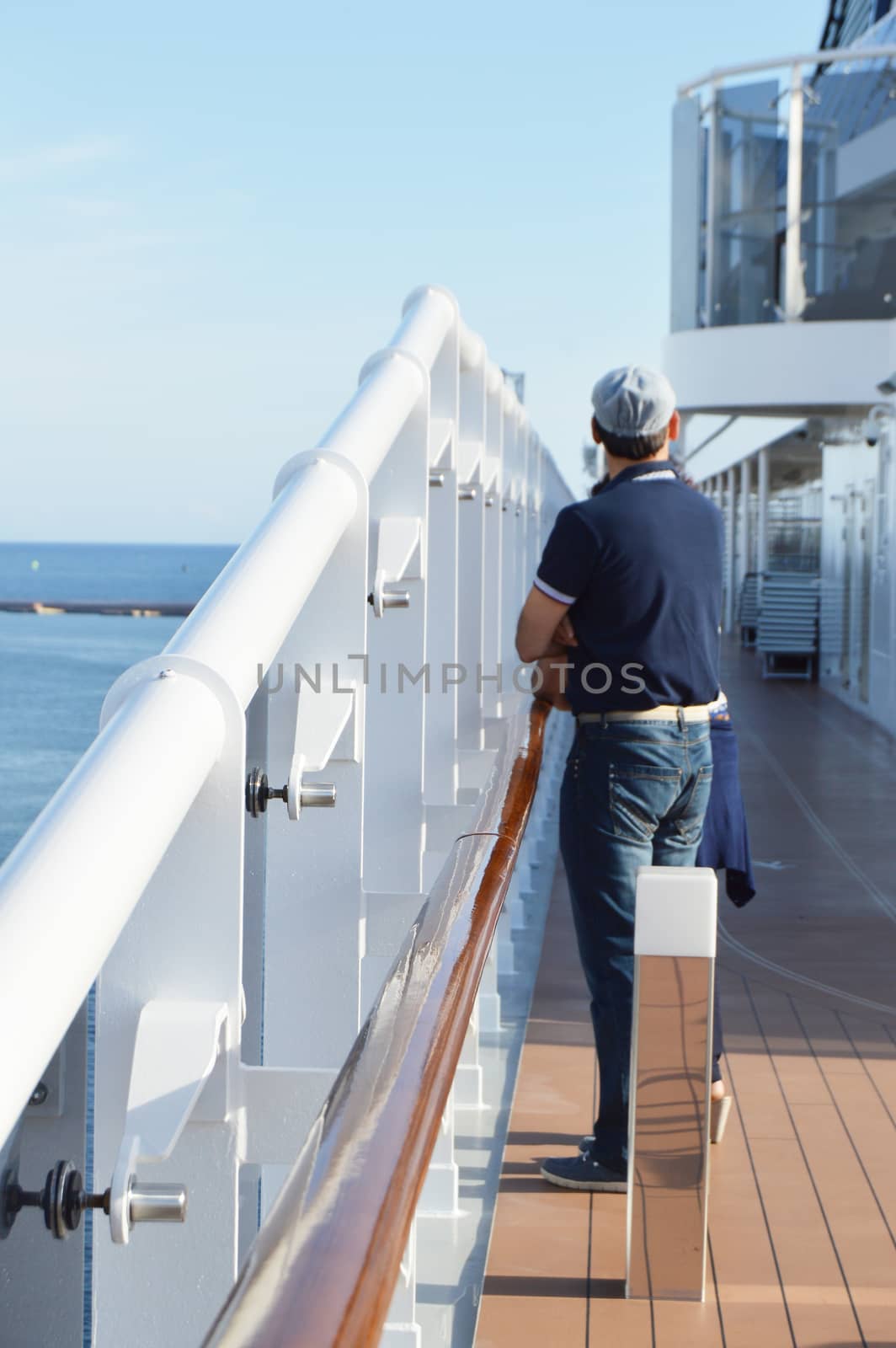 A man standing on the deck of a cruise ship and looking at the shore on a Sunny day, vertical shot by claire_lucia