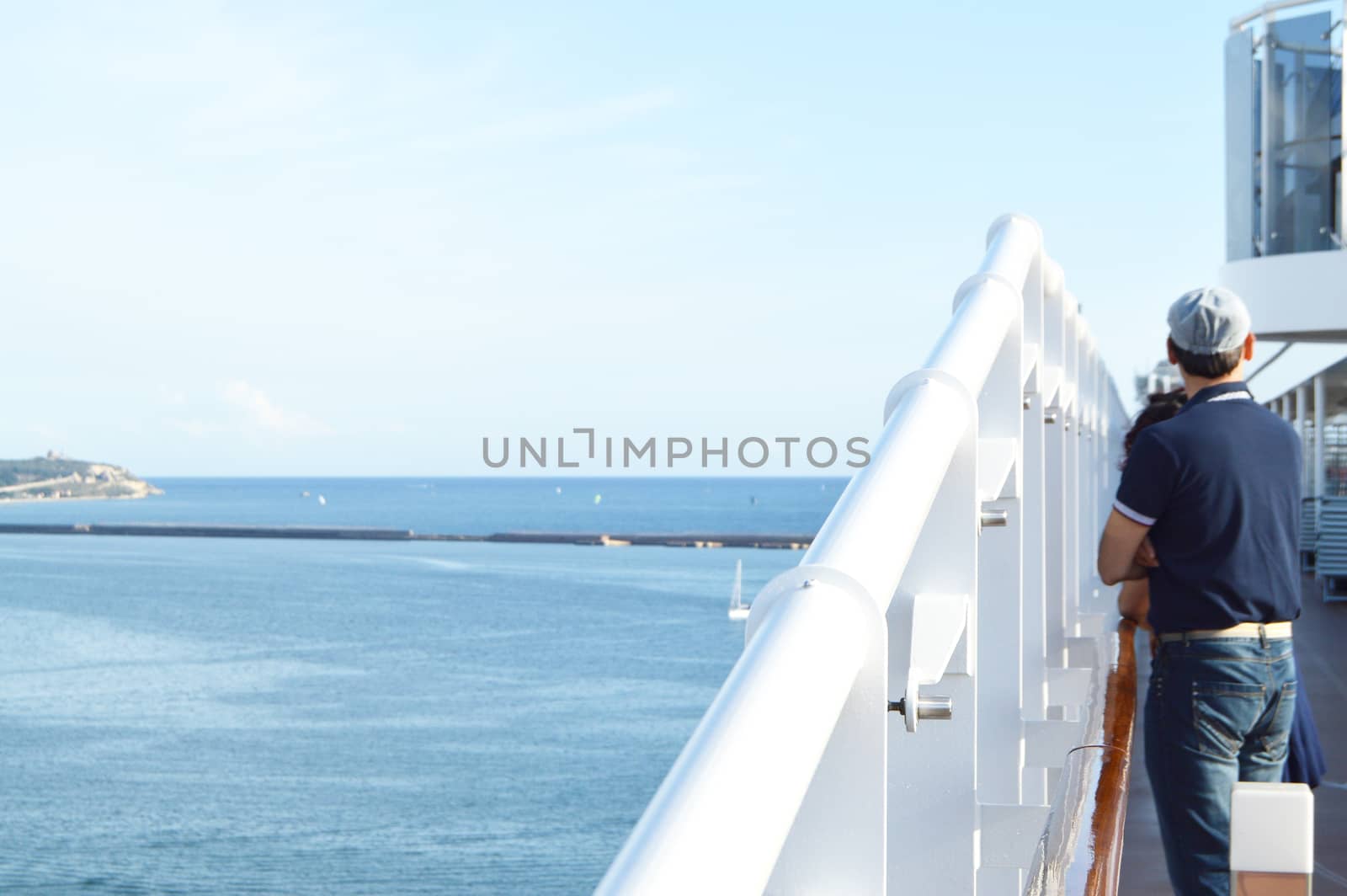 A man stands on the deck of a cruise ship and looks at the shore on a Sunny day by claire_lucia