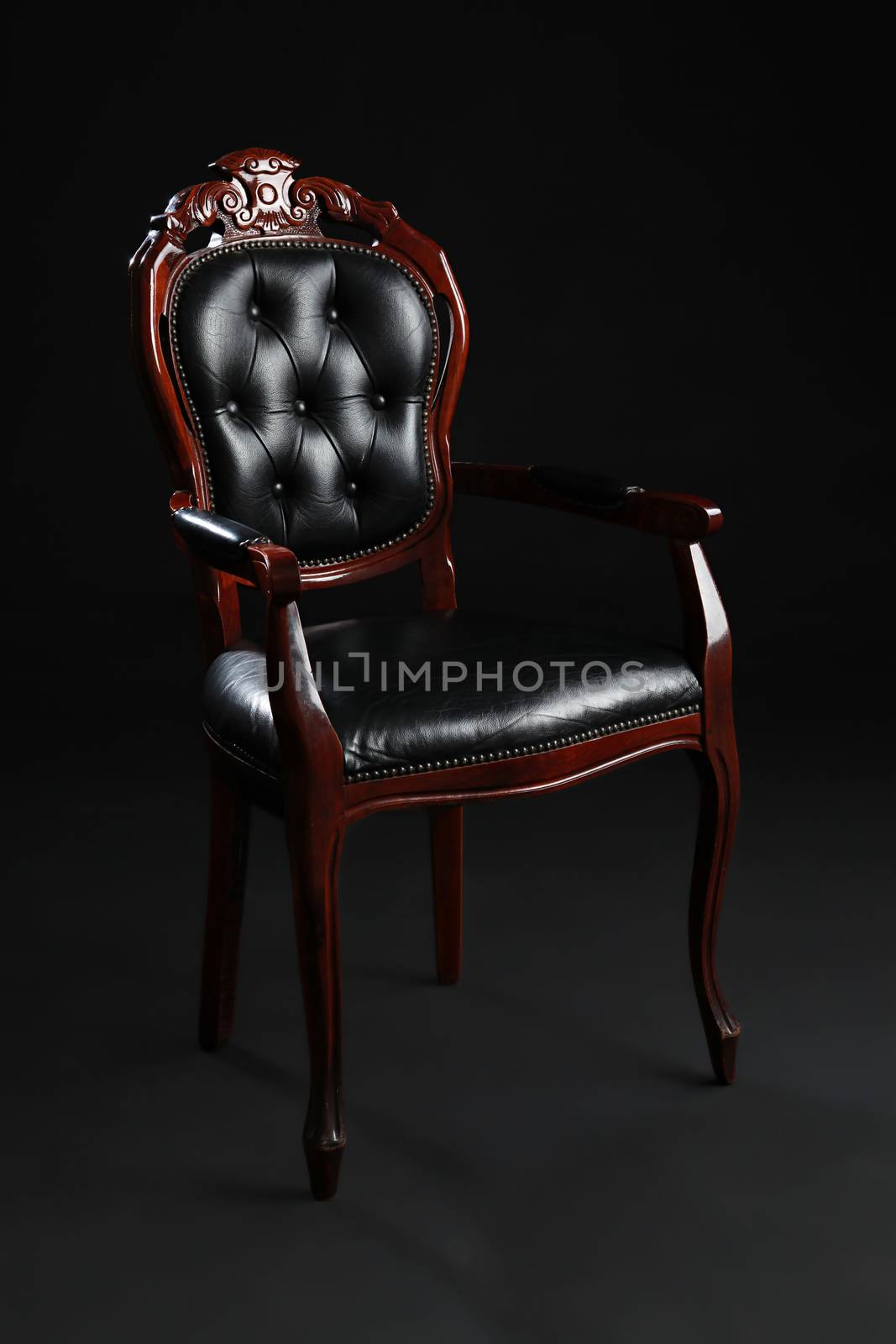 Old black chair, upholstered in leather on black background.