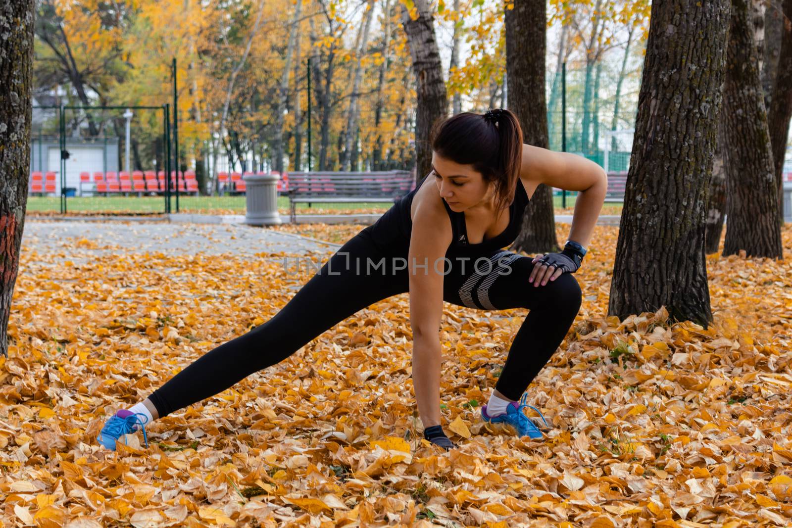 Khabarovsk, Russia - Oct 07, 2018: An attractive woman in sports clothes doing sports exercises in nature against the sunset and the Amur river, loves gymnastics, kneads her legs. Active young girl engaged in sports, leads a healthy lifestyle. by rdv27