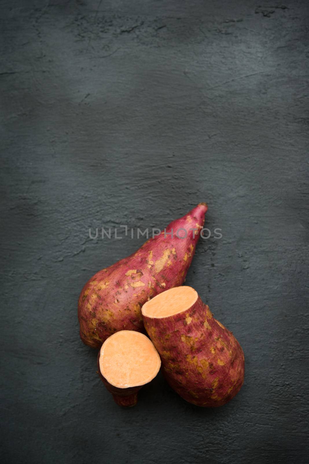 Raw orange sweet potatoes over dark table. Copy space top view.