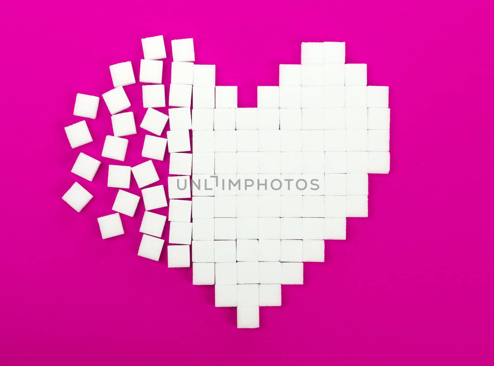 Broken heart made of sugar cubes lies on a trendy pink background