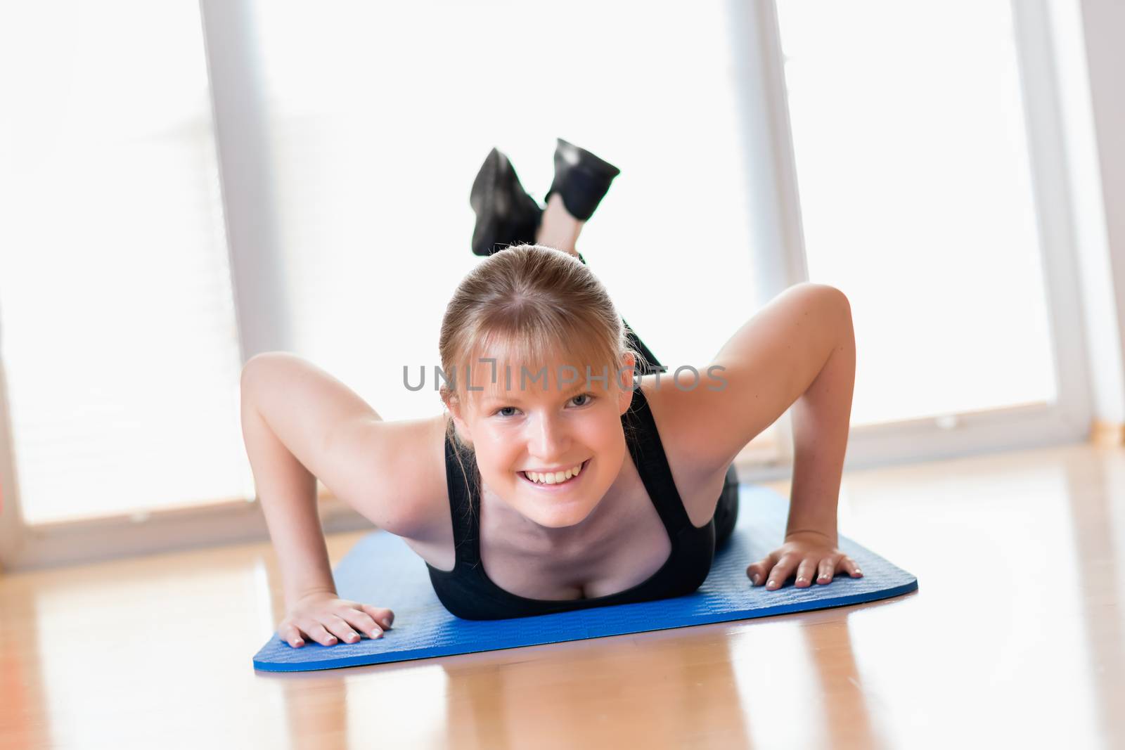 Happy young girl doing pushups exercises on the floor at home