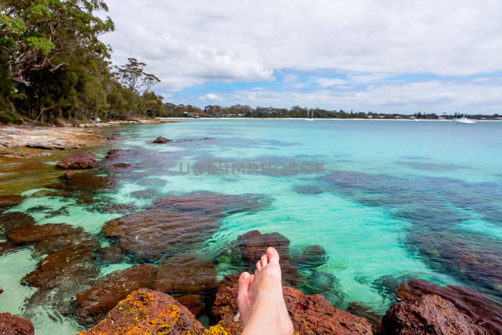 Relaxing on rocks in crystal clear waters, a beach paradise, yachts and boats moored offshore