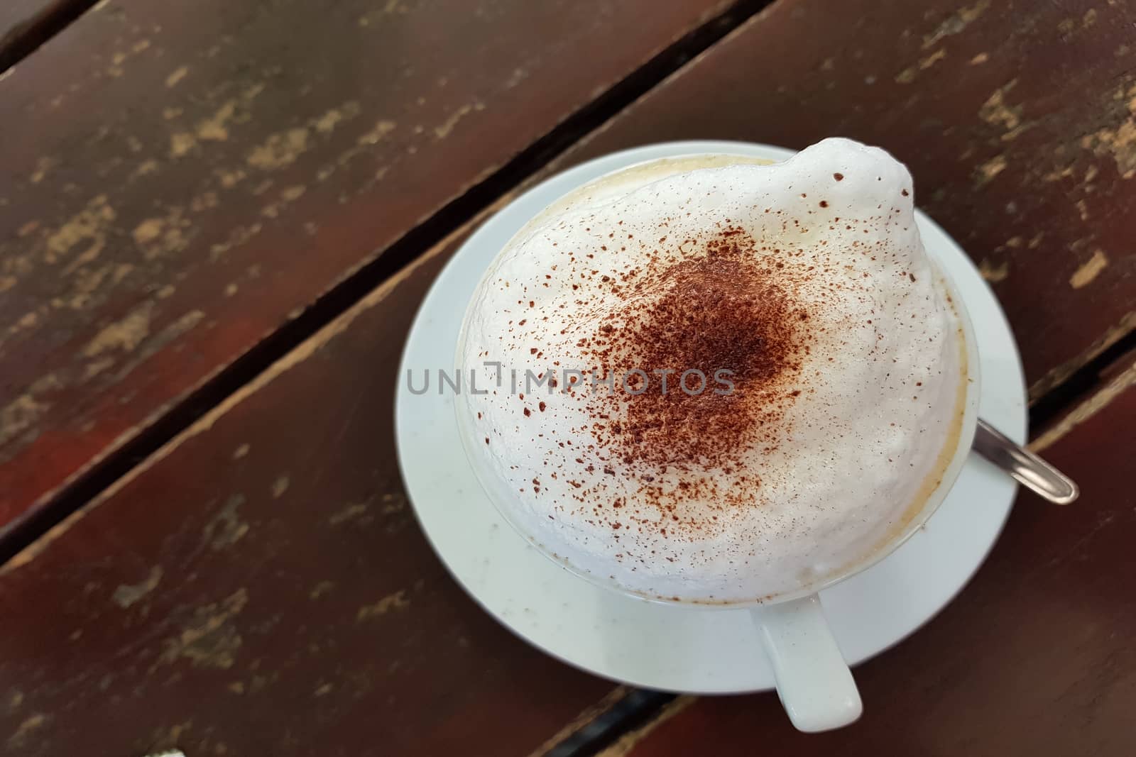 Closeup on a plain white coffee cup with milk foam after latte style on brown wooden table top in a cafe.