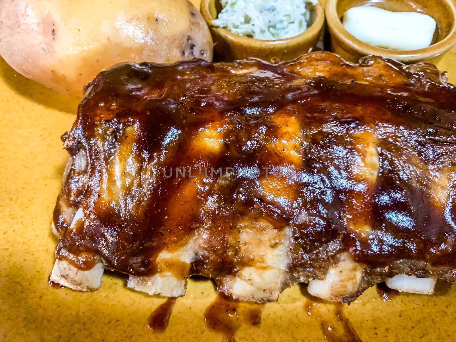 A close view of pork ribs with bbq sause with baked potato, and bows of sauces