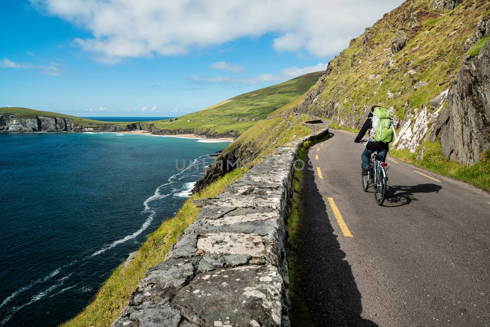 A cyclist riding his bike in the early morning. The road is in the middle of the mountains and the coast in Ireland.