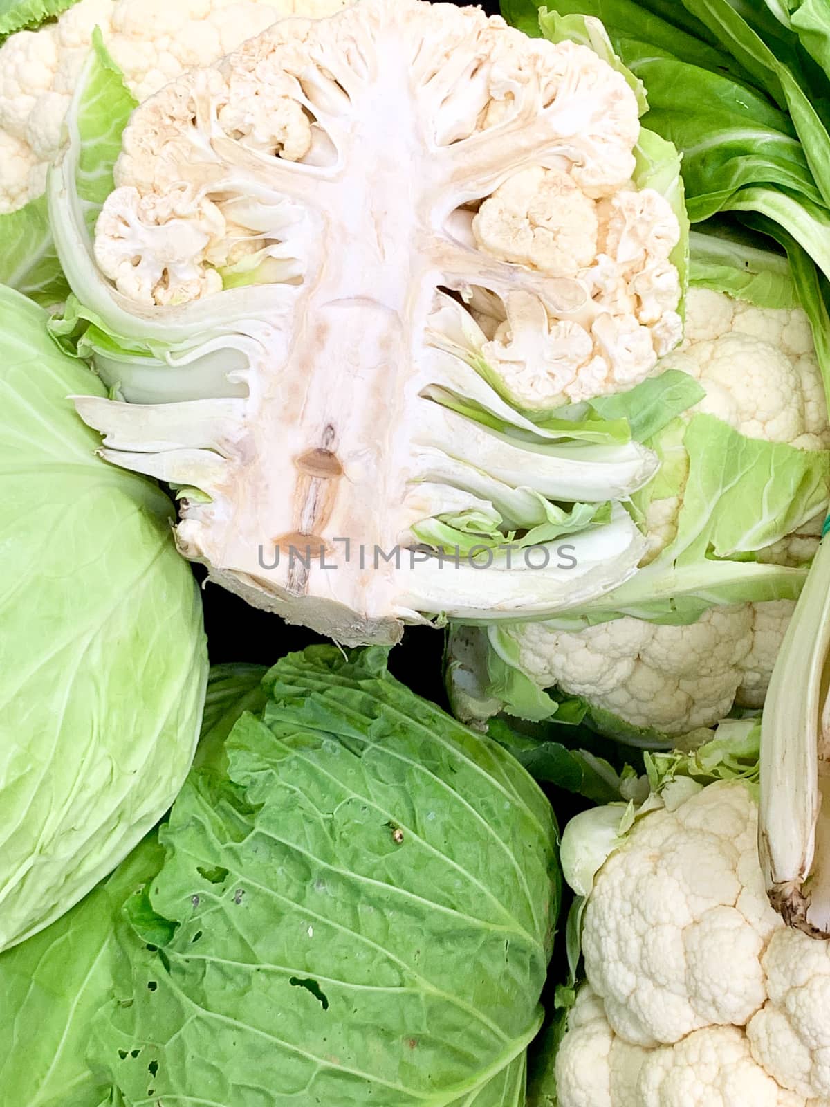 A close up of fresh cauliflowers cut in two and entire. The intense green colour od the leaves in contrast of the white of the cauliflower.