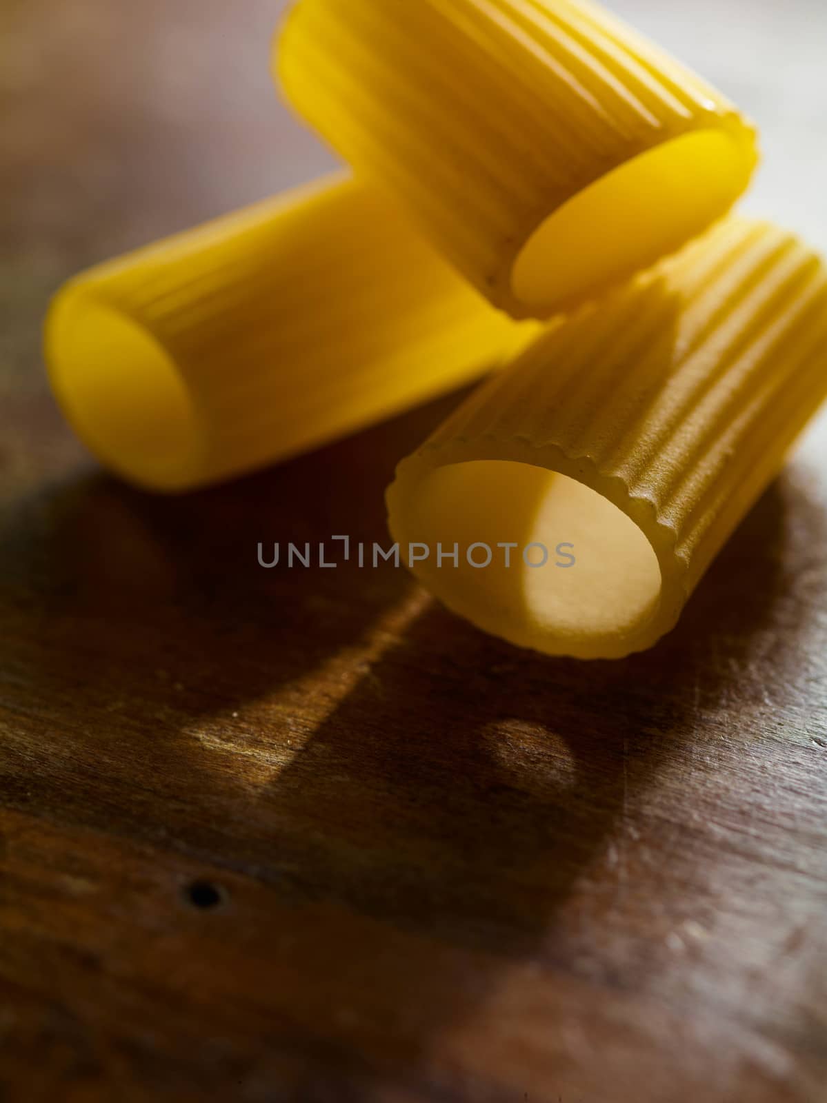 Beautiful contrast of the intense yellow color of rigatoni pasta and the brown wooden table. Detailed closeup