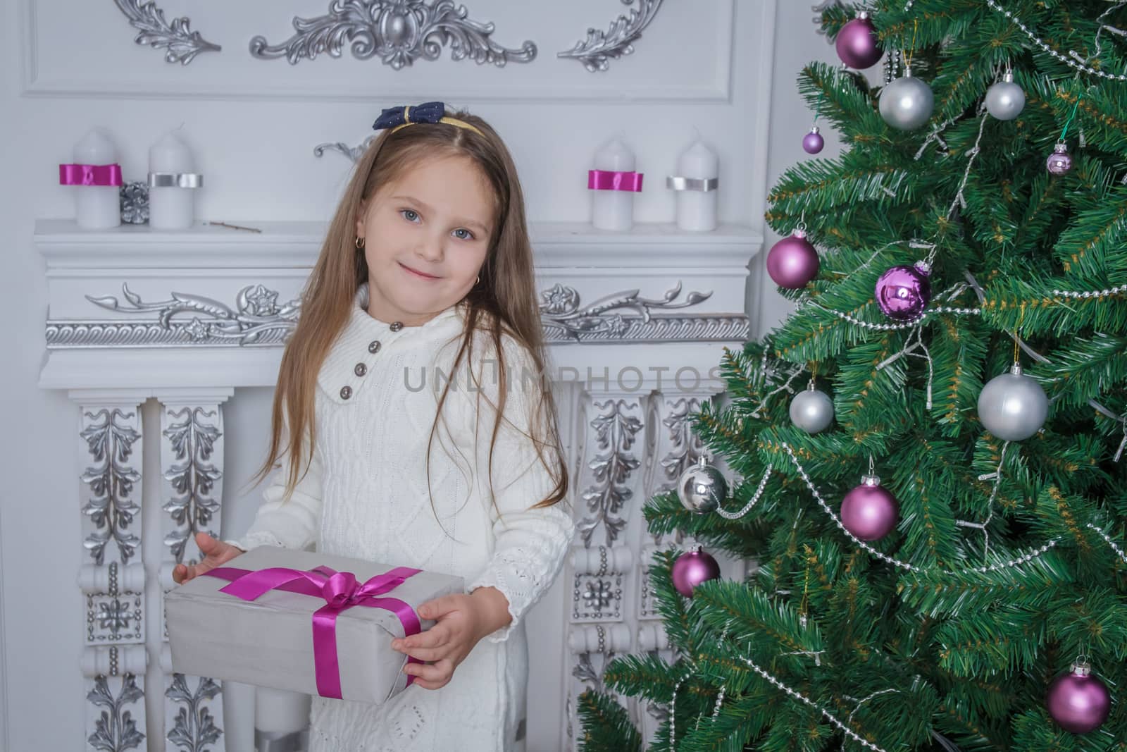 Cute smiling little girl iwith gift box near Christmas tree