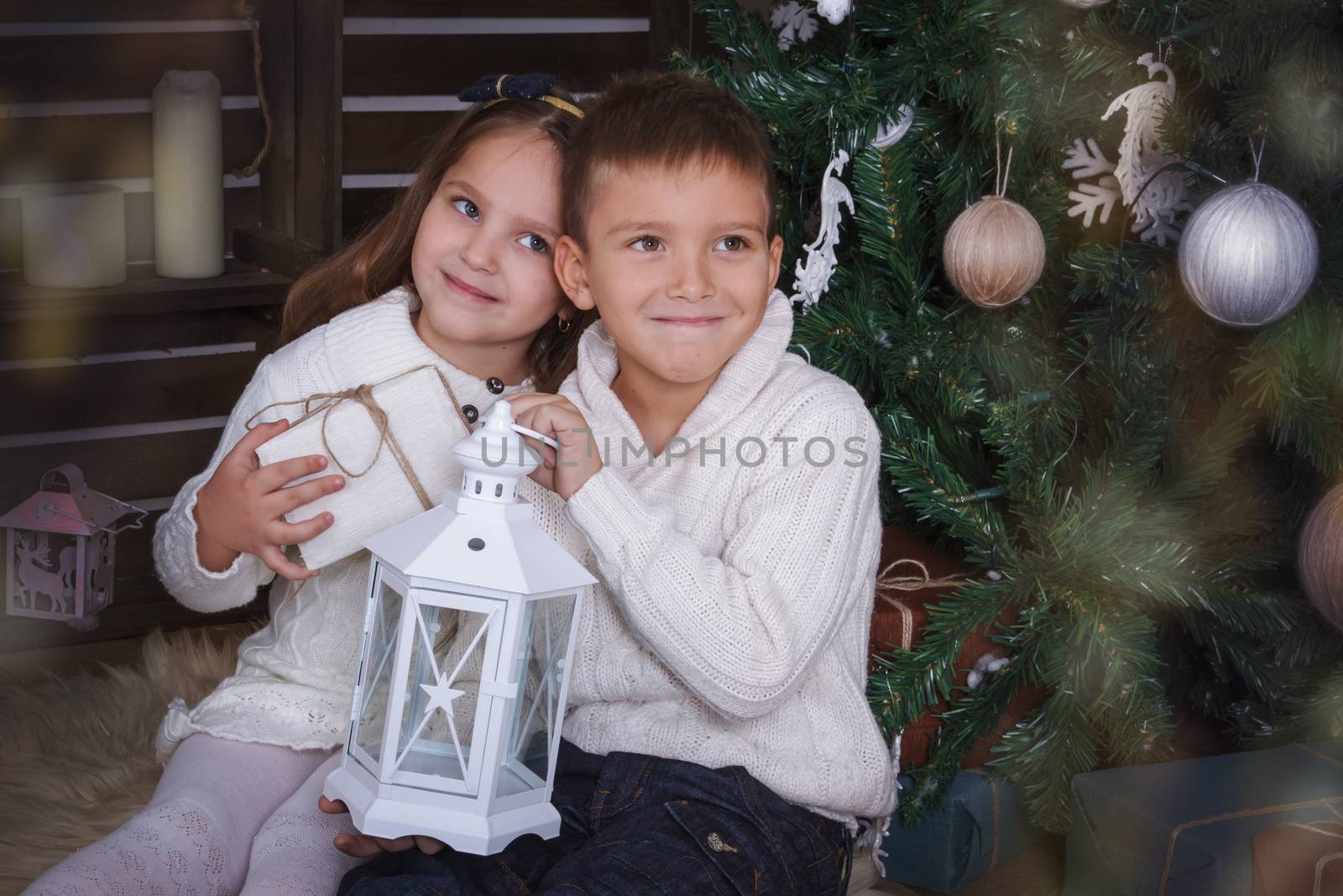 Sister and brother sitting under Christmas tree with gift and lamp