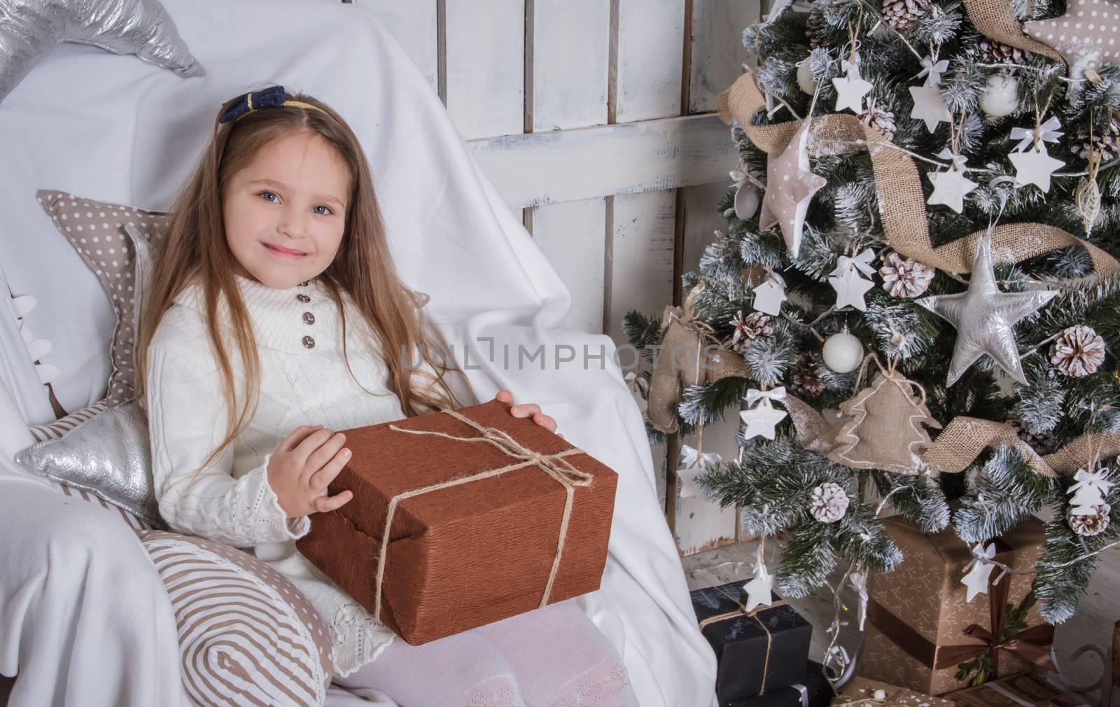 Smiling cute girl with Christmas gift sitting on chair