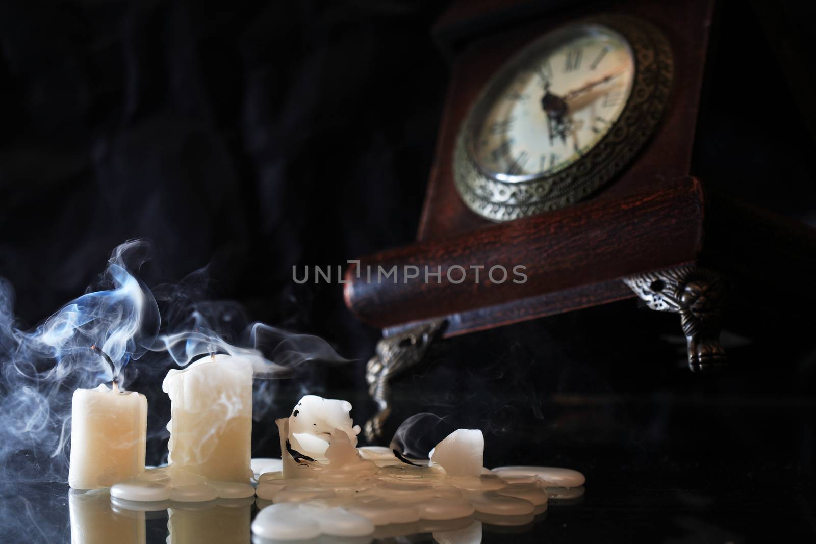 Set of extinguished candles near old clock on nice dark background