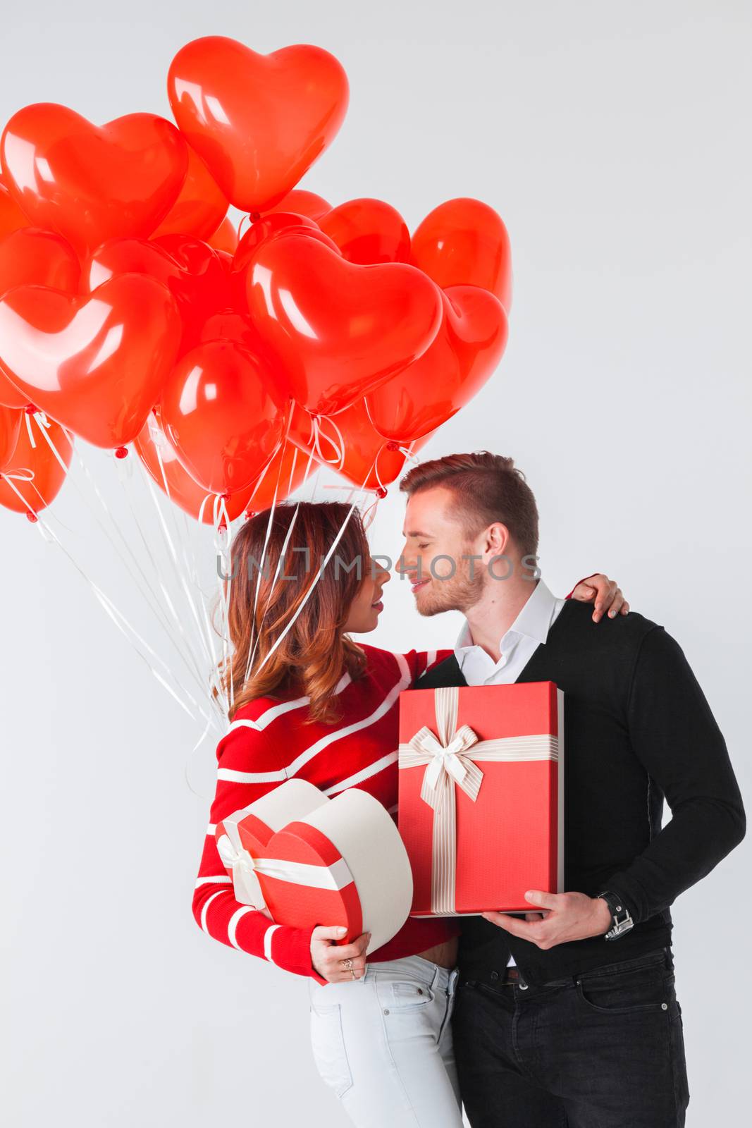 Happy kissing couple in love holding Valentines day gifts and bunch of heart shaped balloons