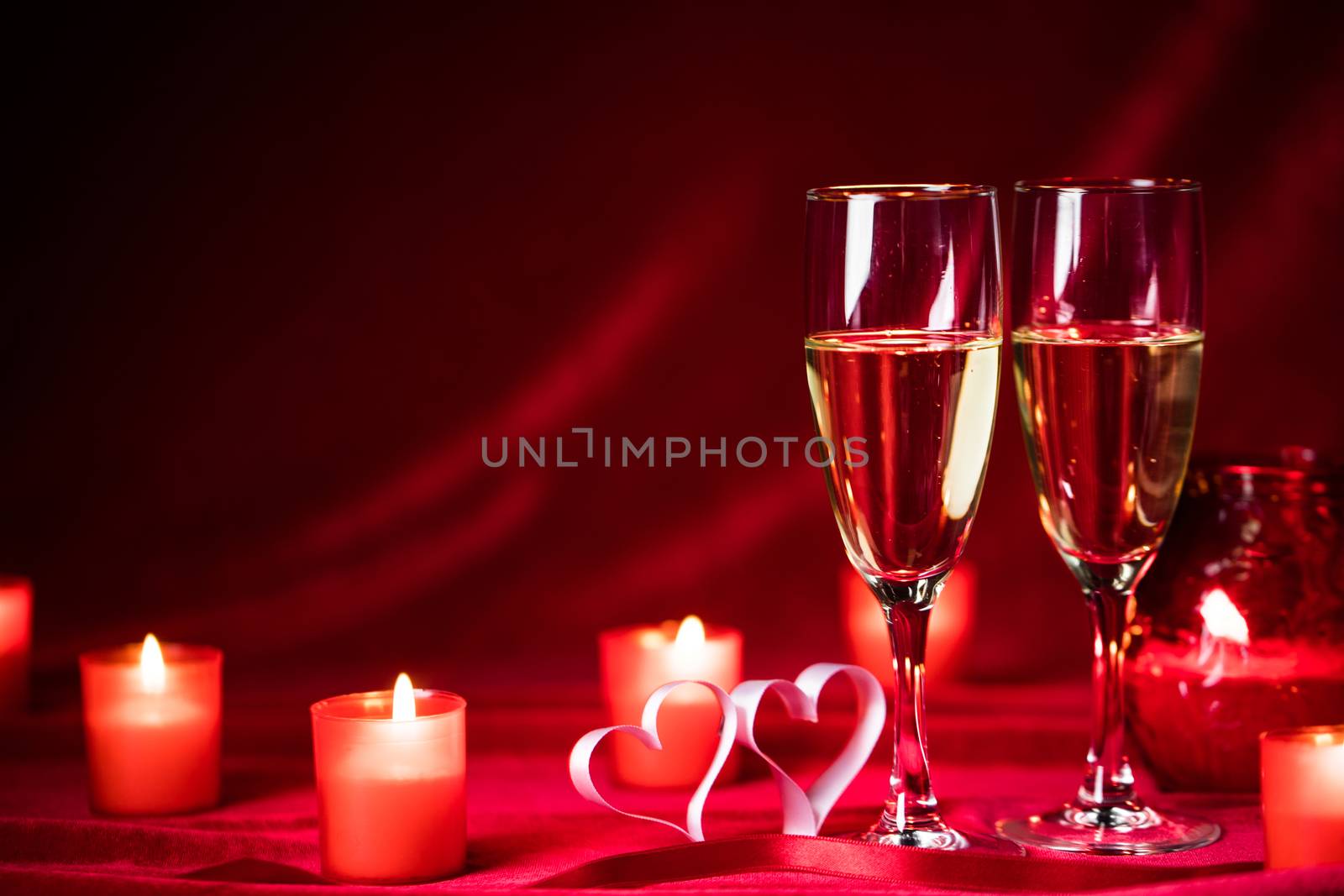 Valentines day celebration, glasses of champagne, candles, roses and hearts on red silk