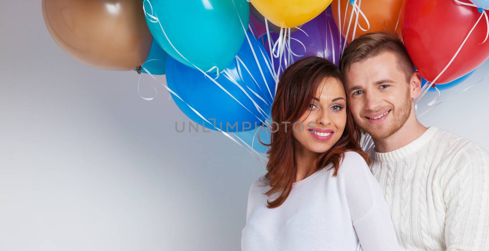 Young smiling couple with colorful balloons on white