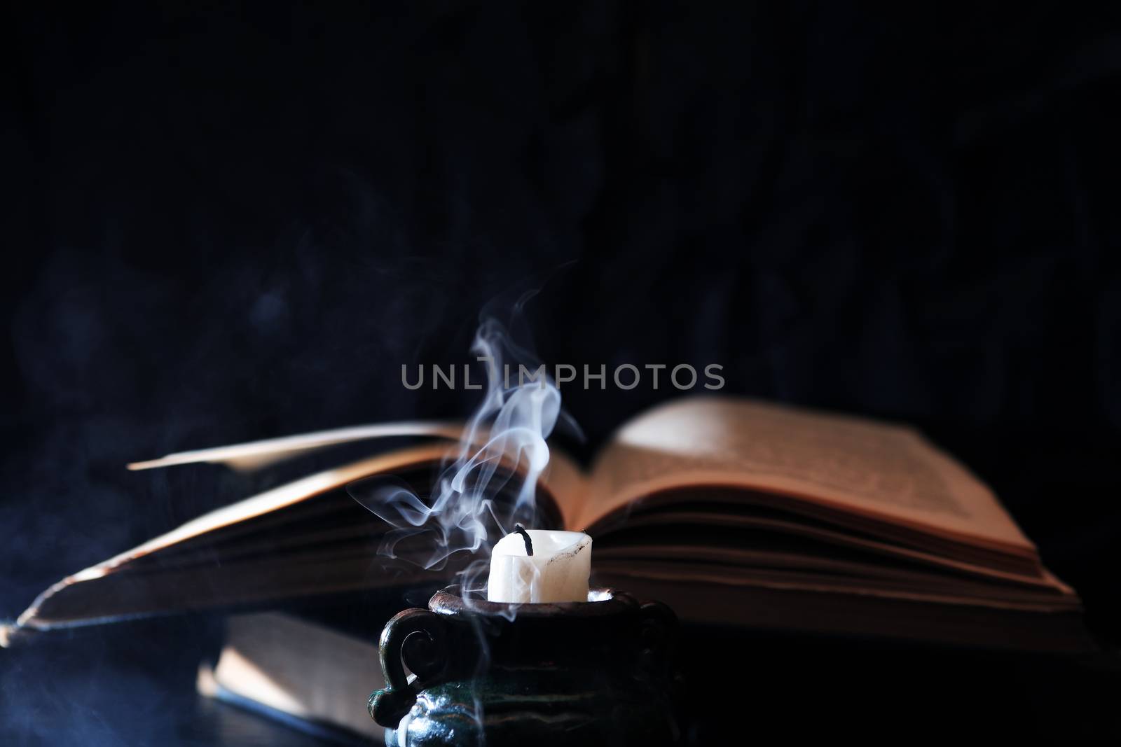 Still life with extinguished candle and blue smoke near old book