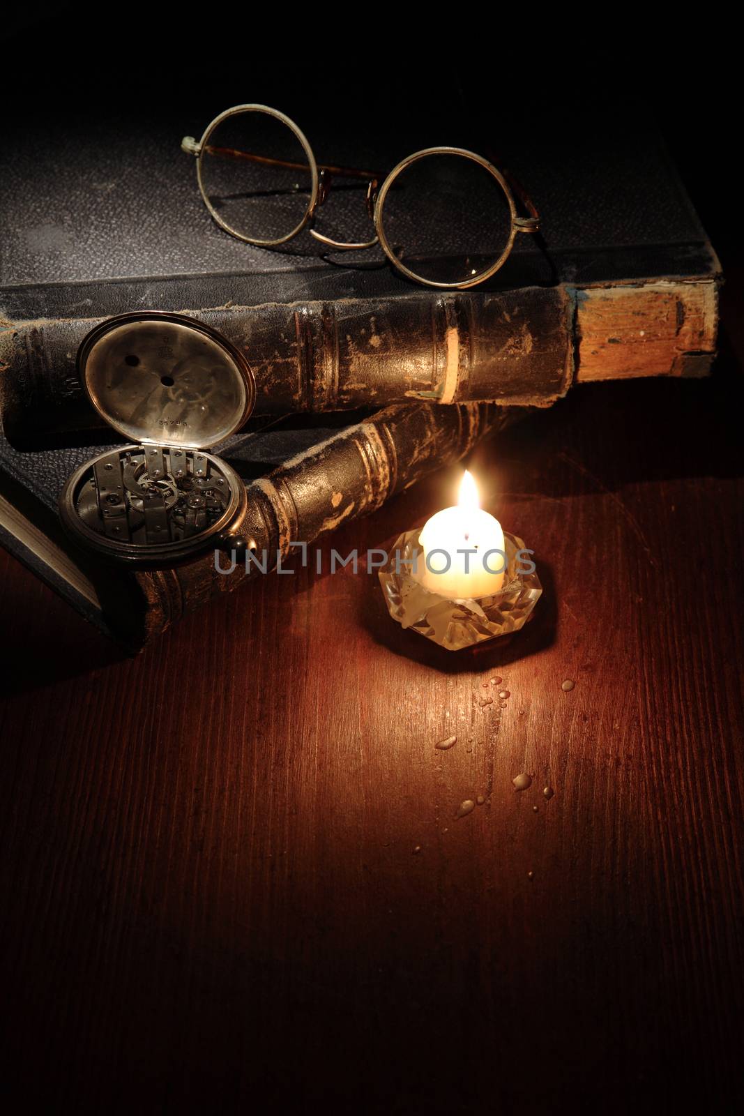 Vintage still life with quill pen and spectacles on old books near lighting candle