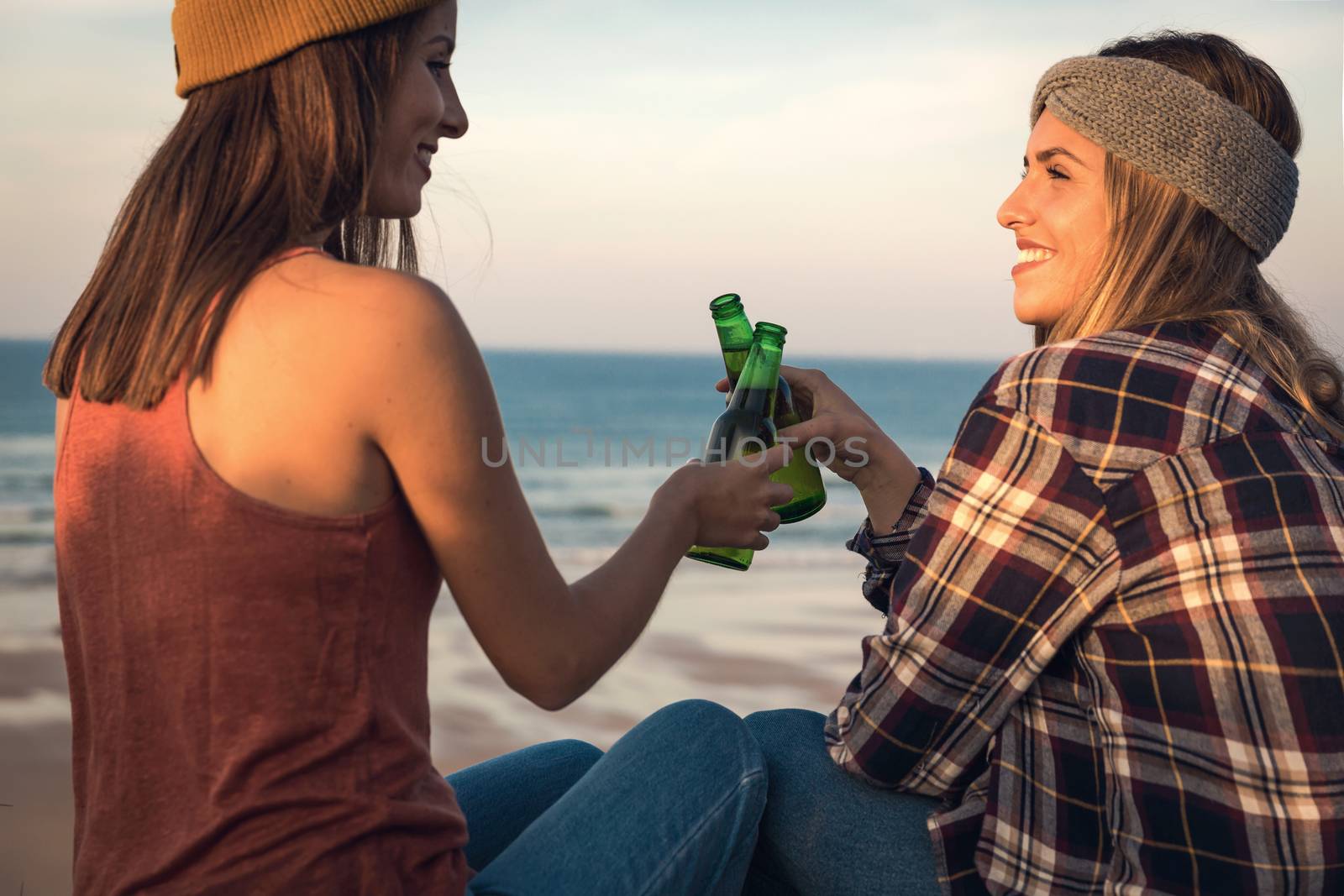 Two best friends sitting on the coastline toasting to friendship