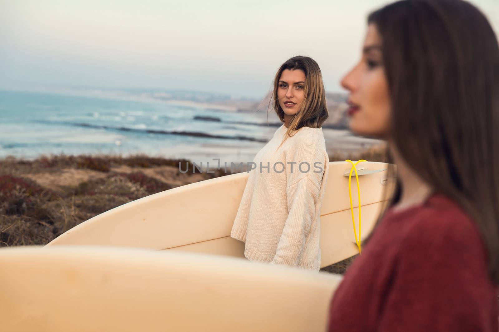 Shot of two female friends holding their surfboards while looking to the ocean