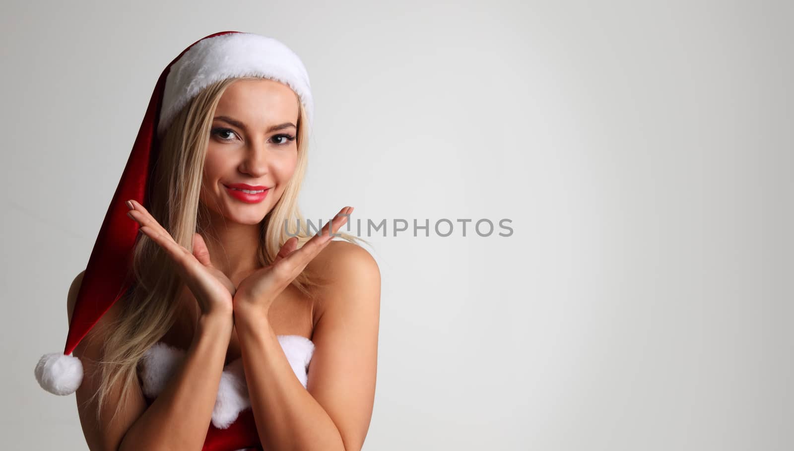 Portrait of a happy attractive young woman posing in red santa claus costume on gray background with copy space