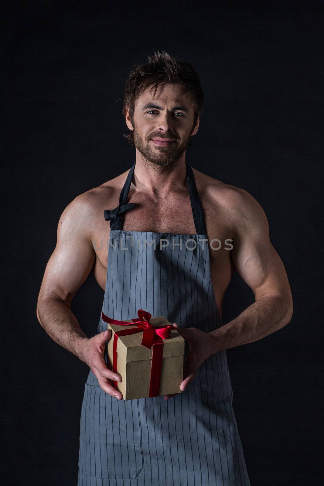 Handsome muscular naked man in an apron holding holiday gift box