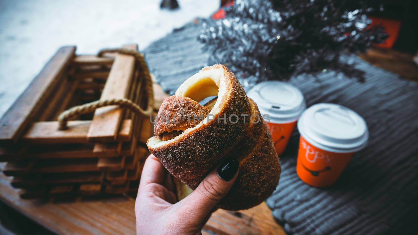 Woman holds in hand Trdlo or Trdelnik, it is a national street street food of Prague on the background of wooden table with glasses of mulled wine