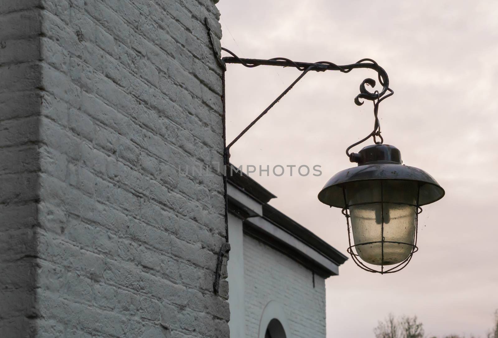 unlit old and dirty vintage street lantern hanging on a brick wall by charlottebleijenberg