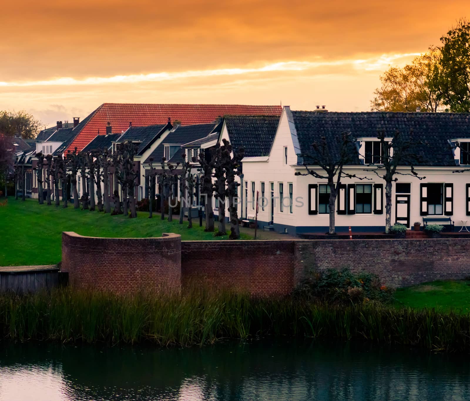 view on some modern houses with water and grass at sunset in the city Leerdam the Netherlands, typical dutch neighborhood. by charlottebleijenberg
