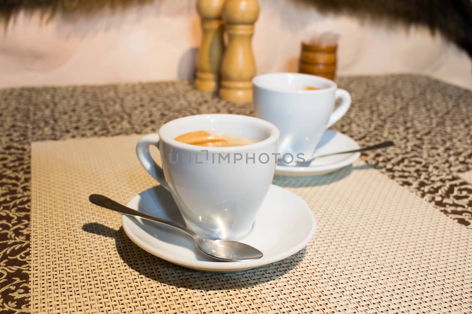 Composition of two cups of coffee on white serving plates with small metal spoons