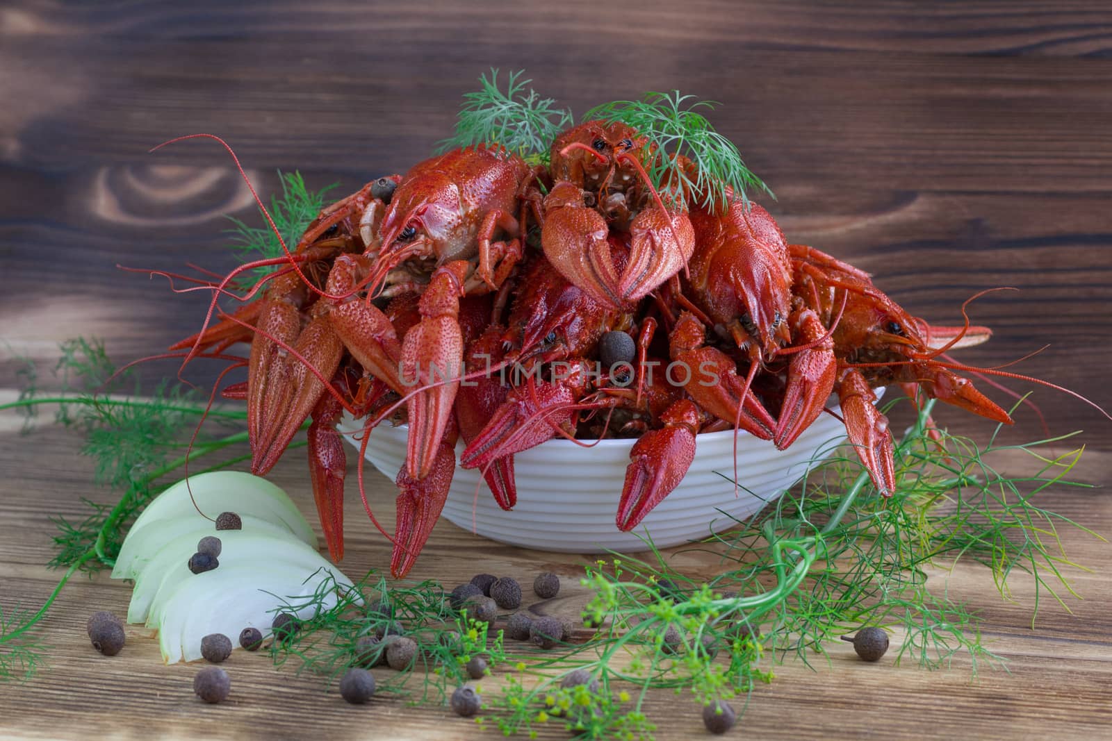 Plate of red boiled crayfishes with claws and fennel, onions and peppers on wooden background