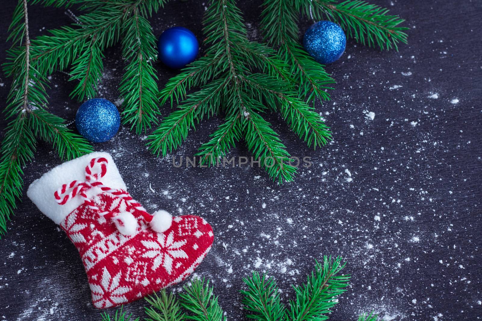 Christmas and New Year winter holiday snowbound composition of red stocking on black space background with green fir tree branches and blue balls ornament