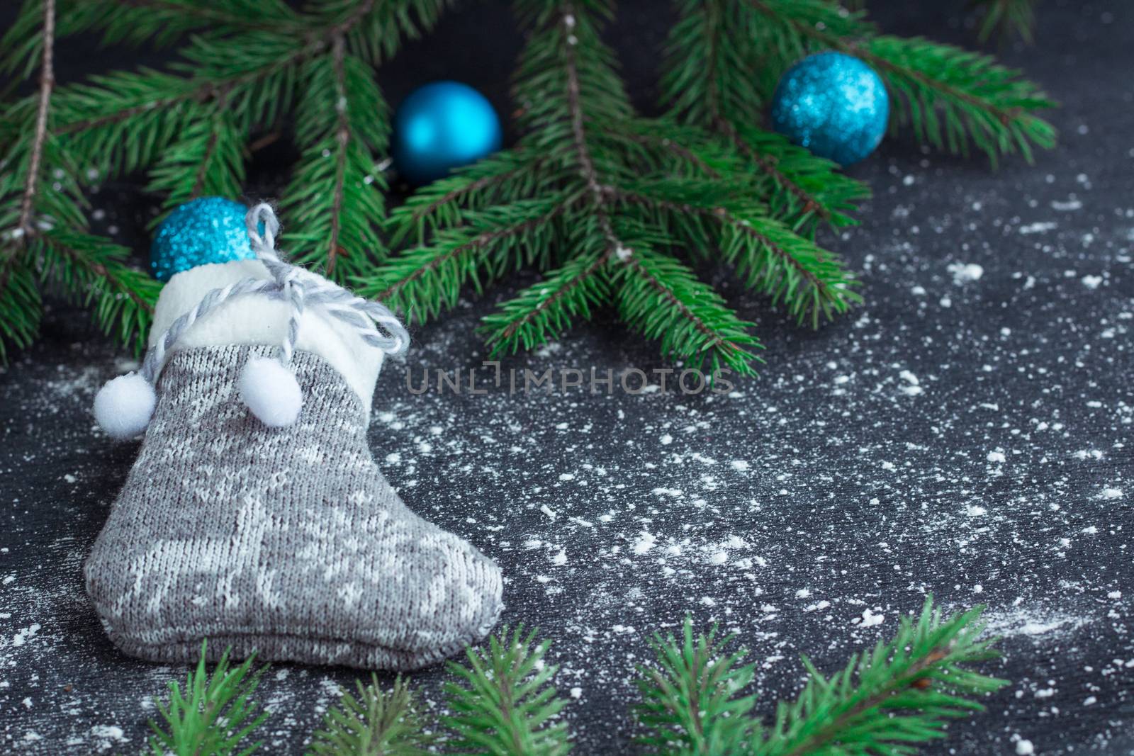 Christmas and New Year winter holiday snowbound composition of grey stocking on black space background with green fir tree branches and blue balls ornament