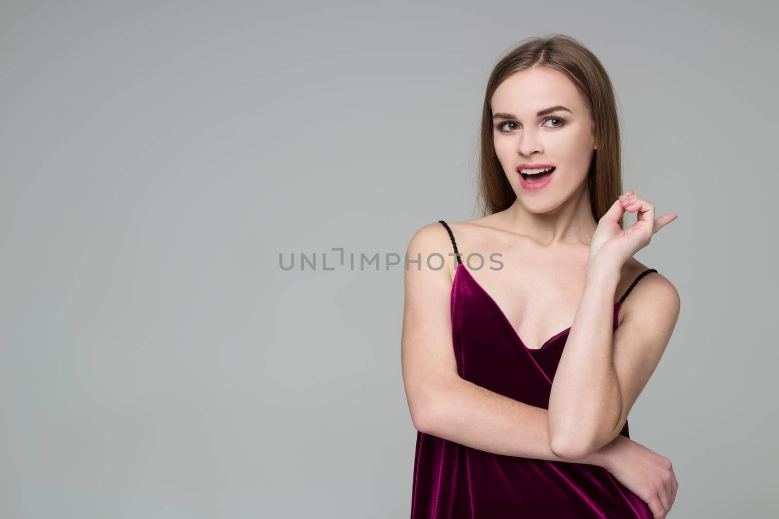 Portrait of posing young model long-haired blond girl in dark red dress showing emotions