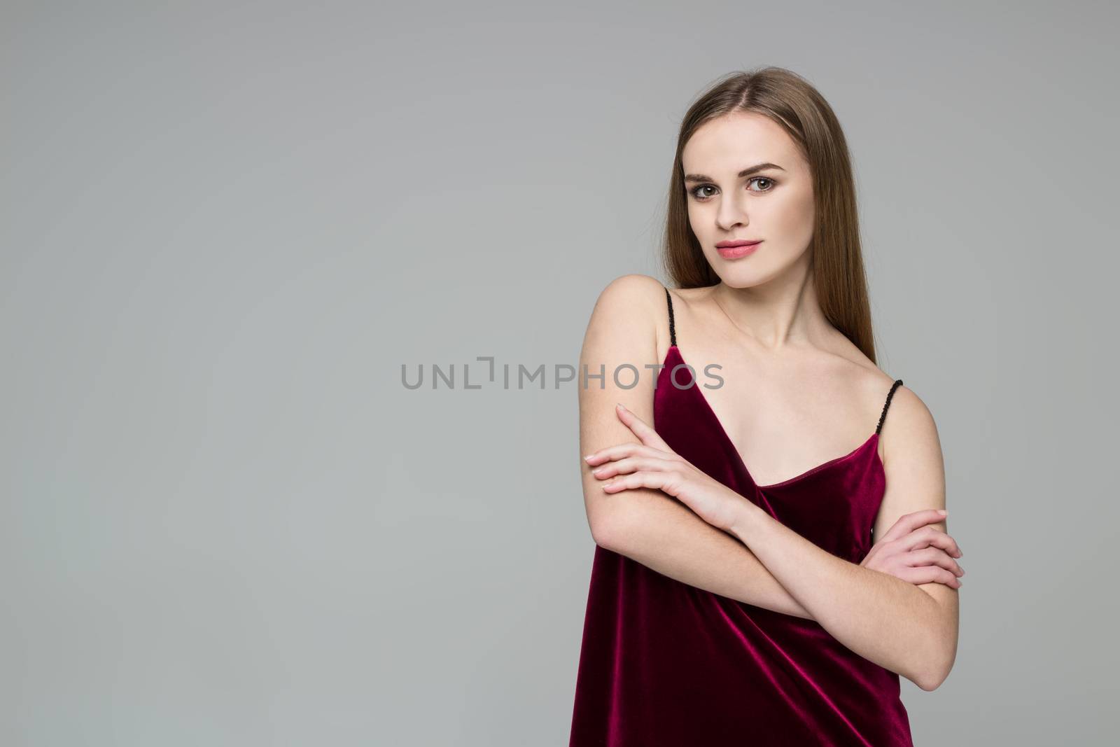 Portrait of posing young model long-haired blond girl in dark red dress showing emotions